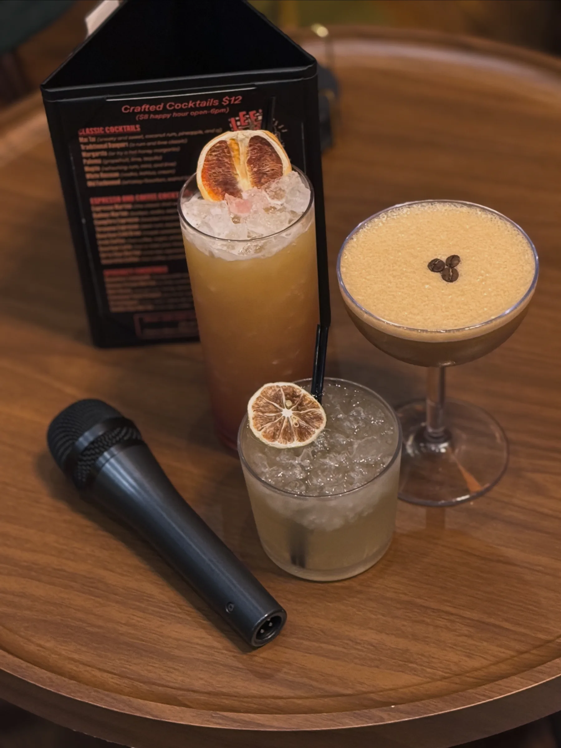 A microphone resting beside three cocktails on a table before karaoke night