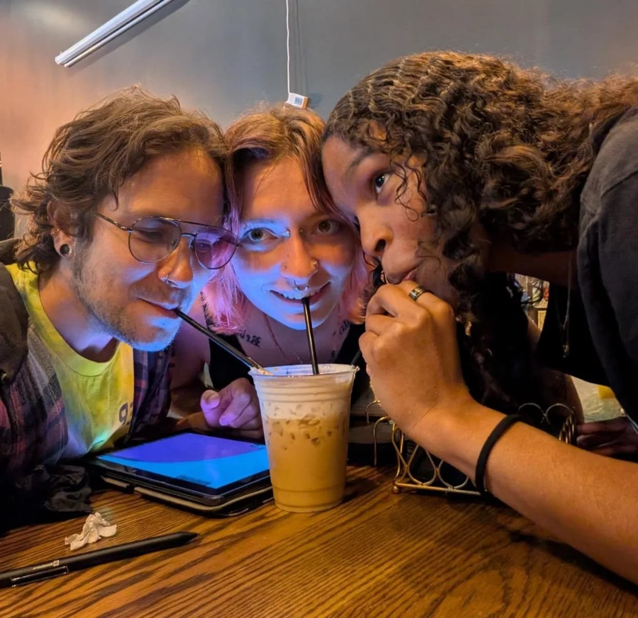 Three friends leaning in to share an iced latte at Lee's Coffee in Birmingham