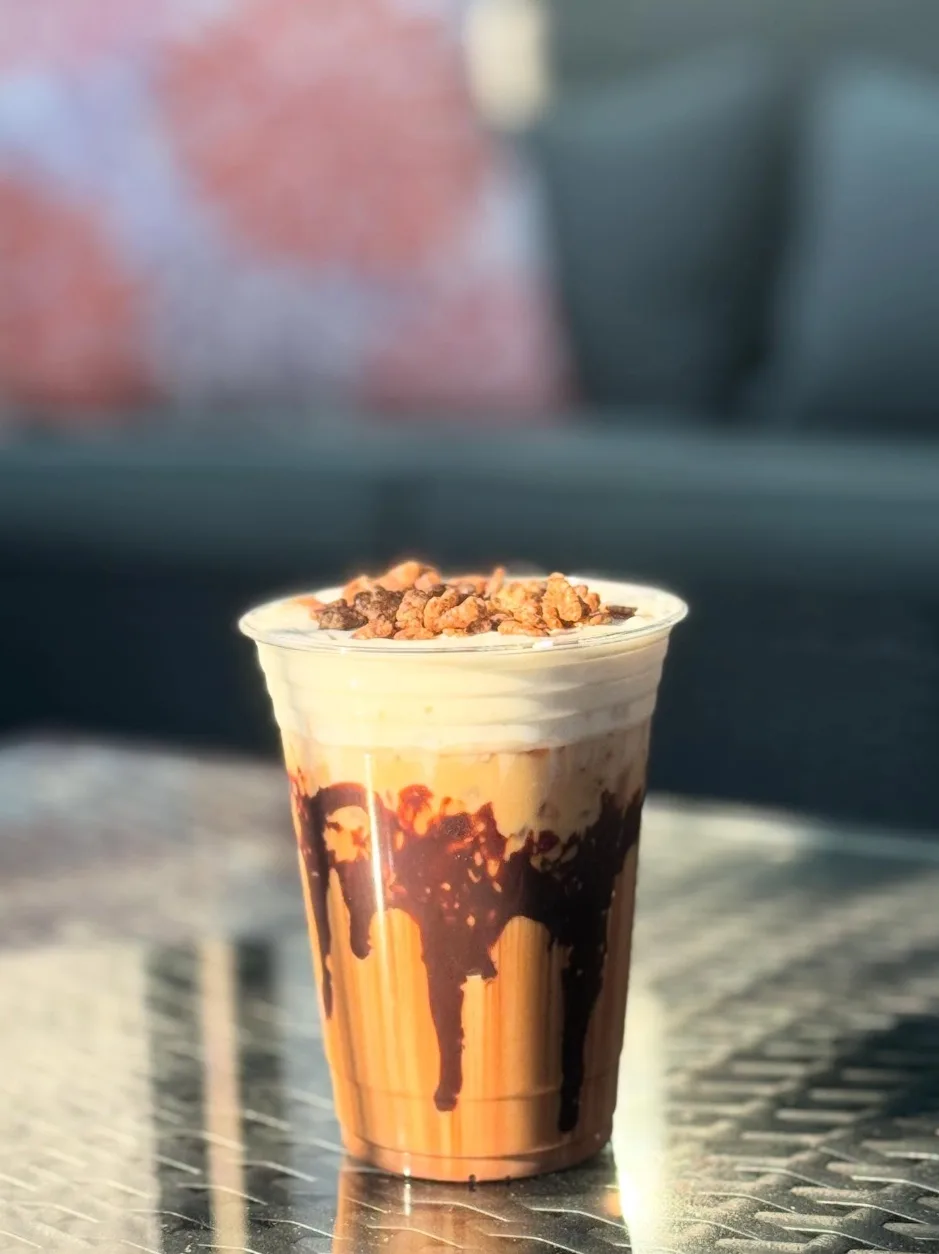 An iced latte layered with chocolate drizzle and toffee crumble on a sunlit patio table
