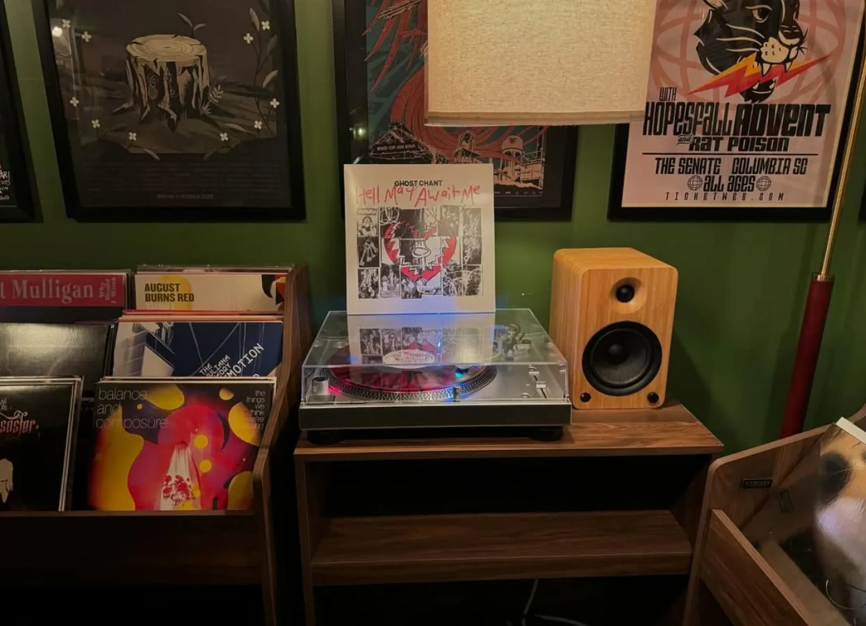 A record player and crates of vinyl beneath framed concert posters on a green wall