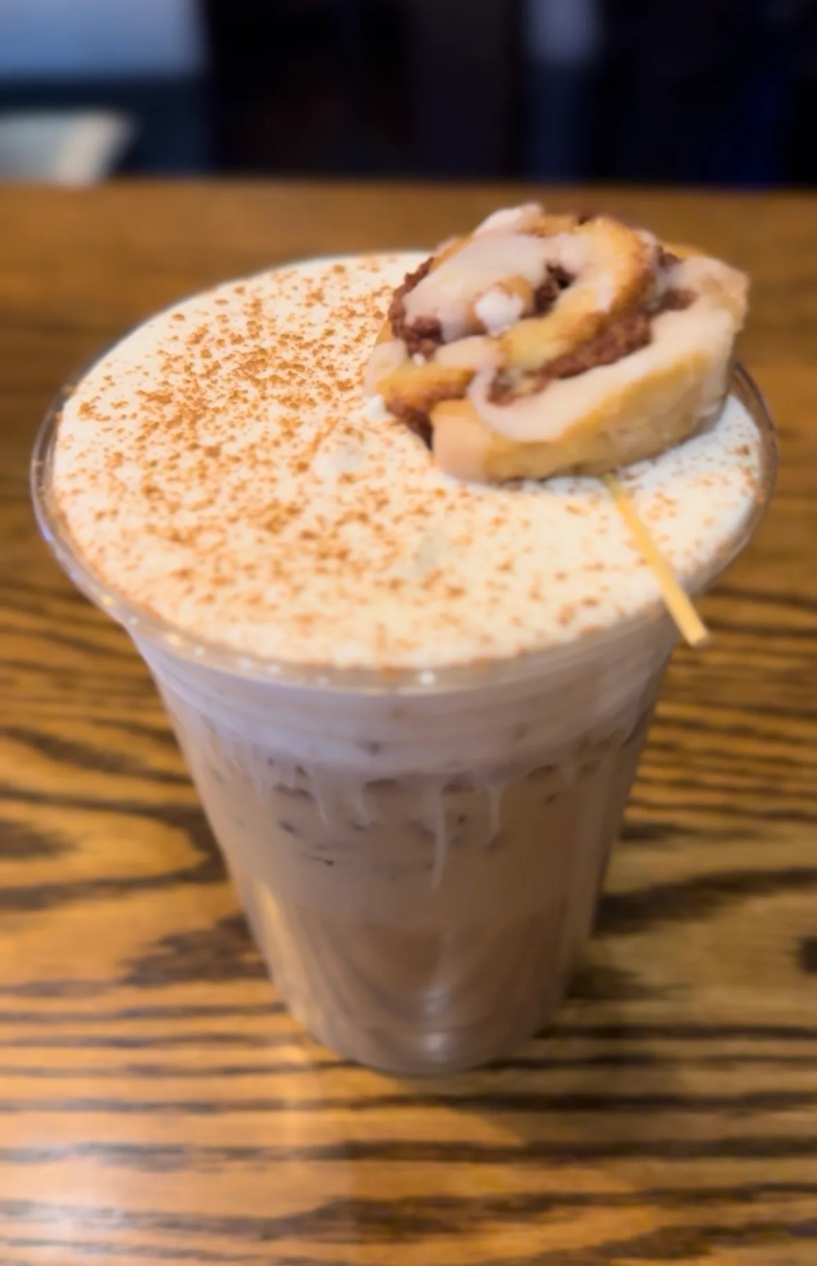 An iced latte with cinnamon cold foam and a mini cinnamon roll garnish
