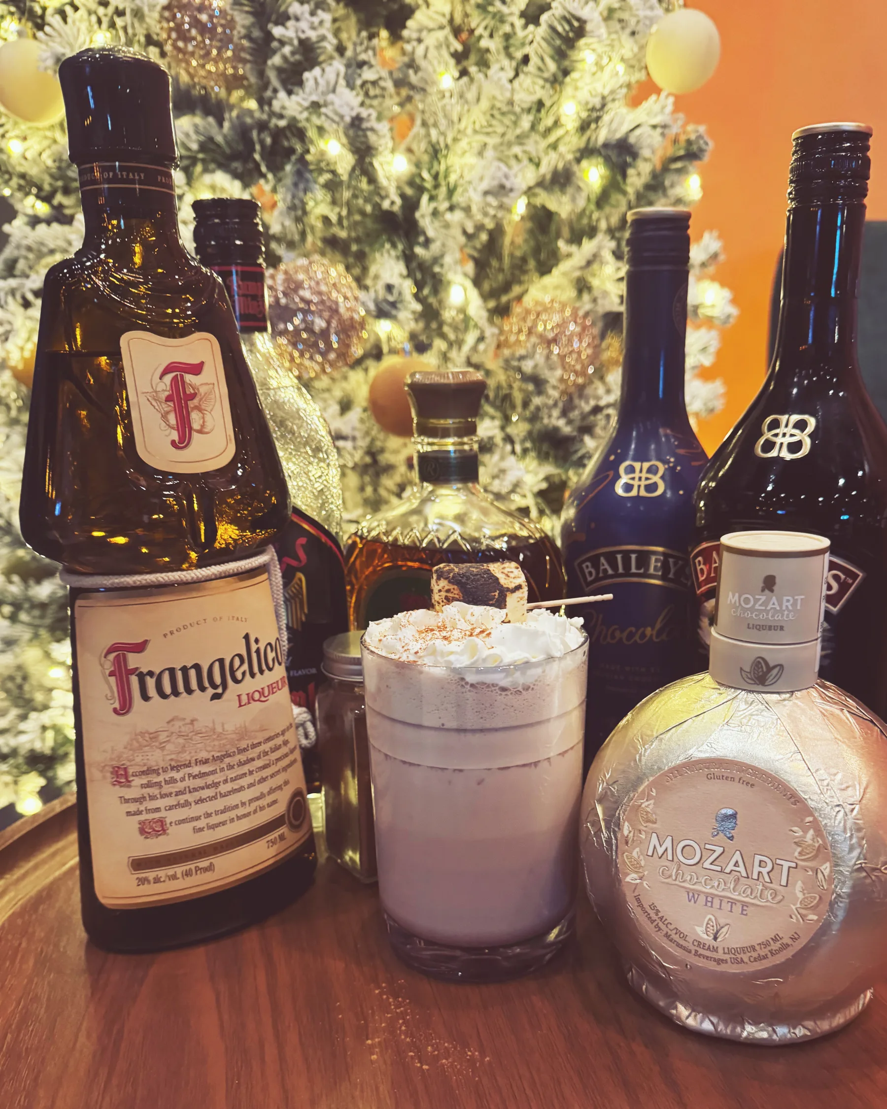 A creamy cocktail with whipped cream and a toasted marshmallow beside bottles at the bar