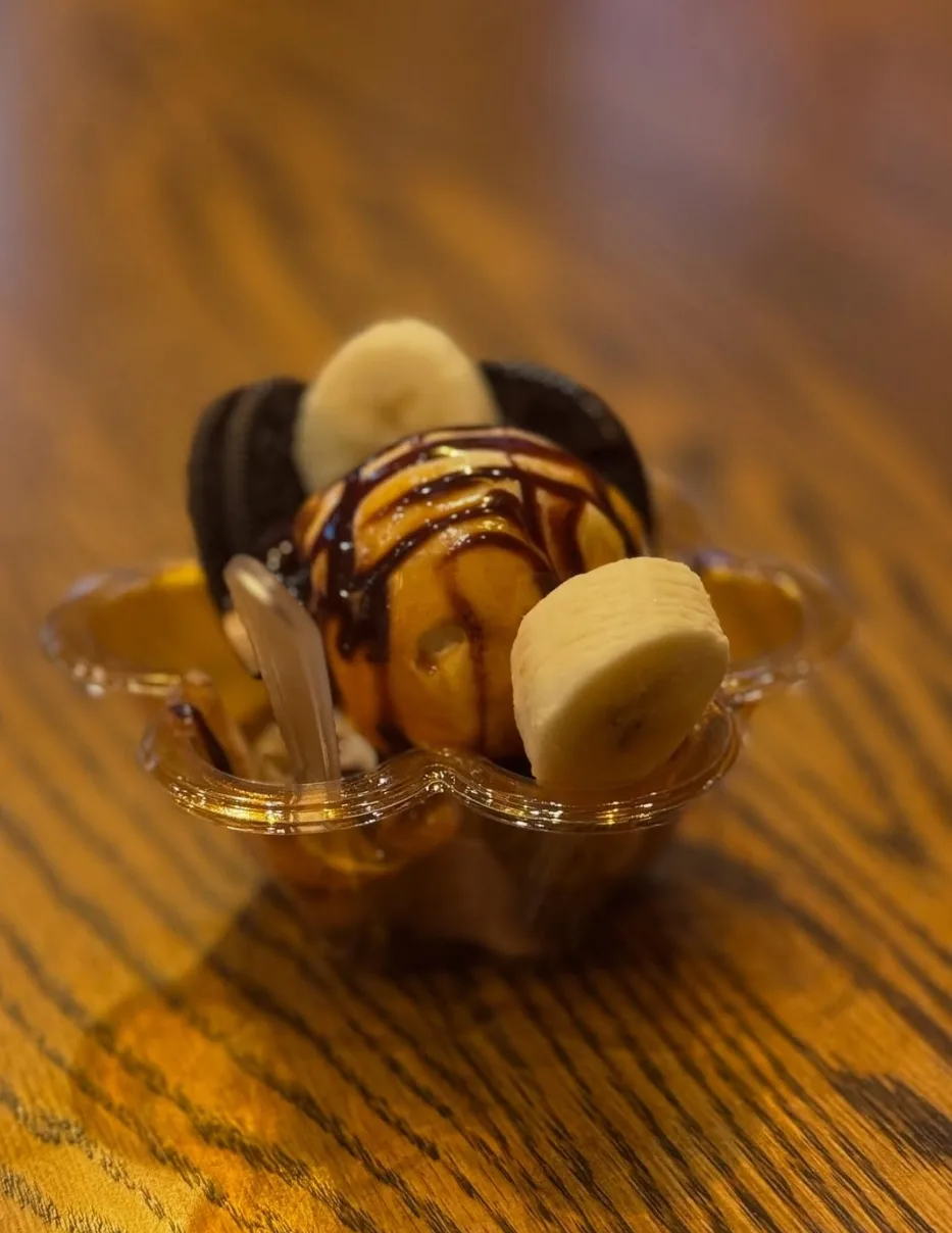 A dessert cup with banana, cookie and chocolate drizzle on a wooden table