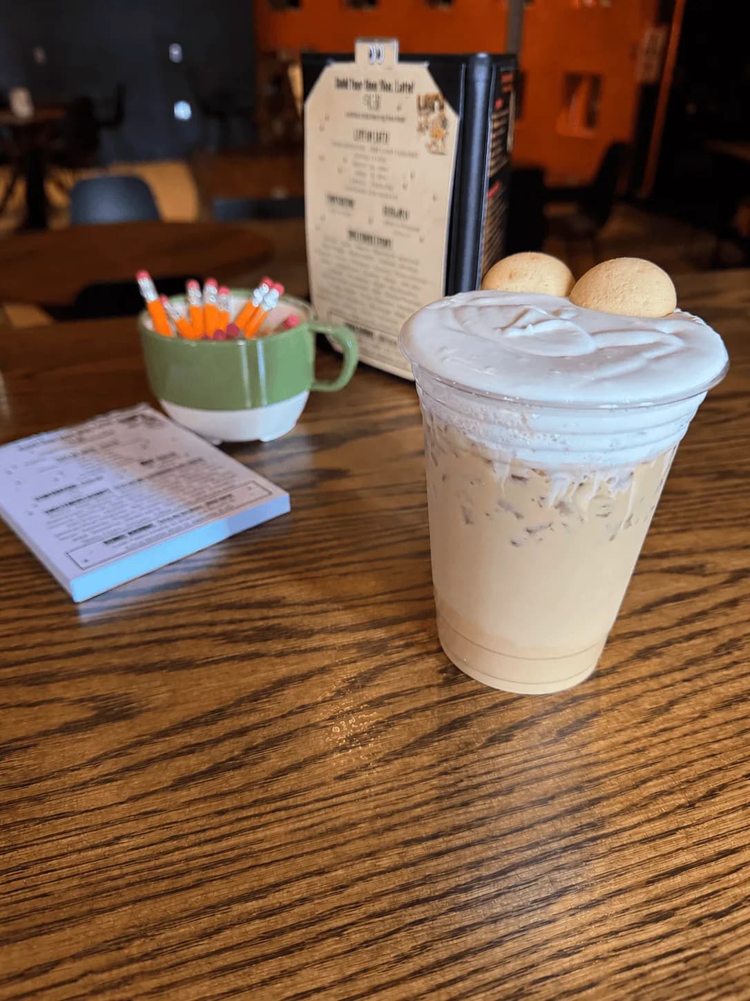 An iced latte topped with cold foam and two cookies beside the Build Your Own Latte menu