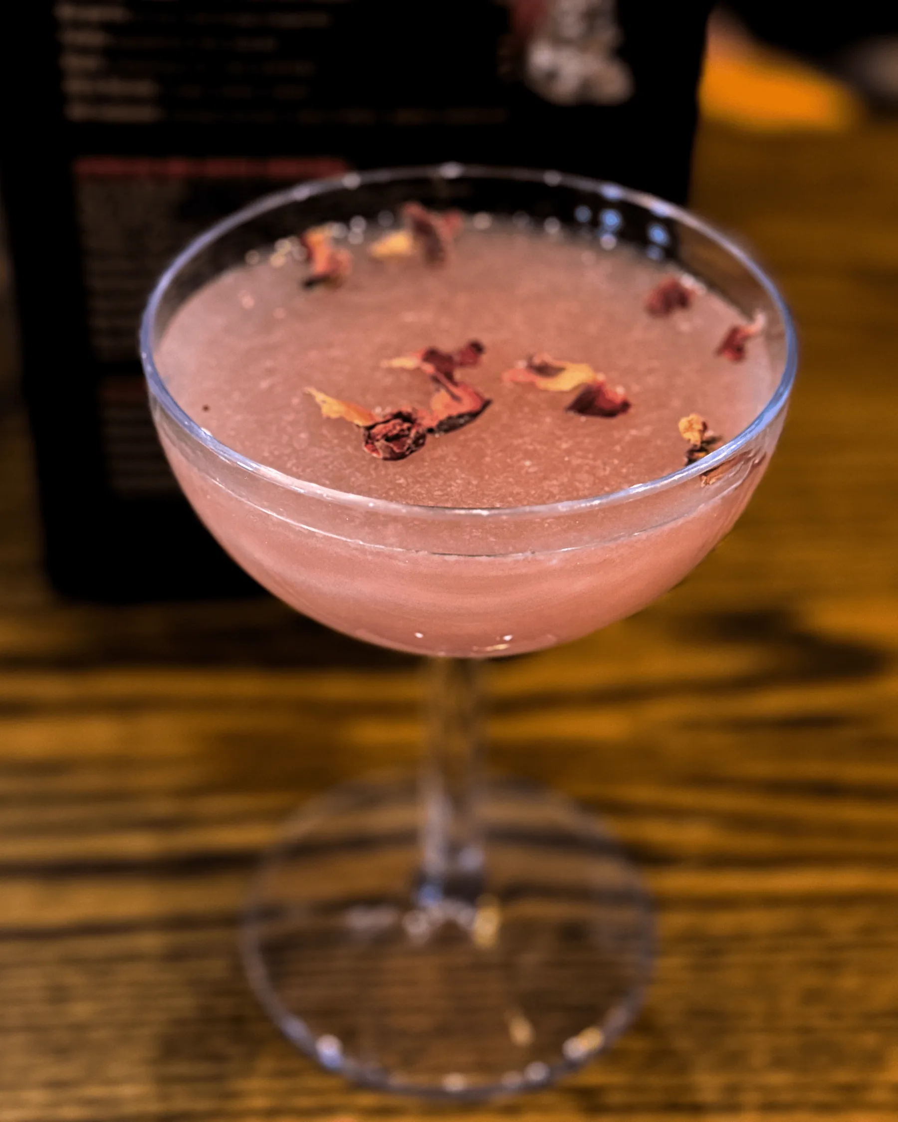 A pale pink cocktail in a coupe glass garnished with dried flower petals