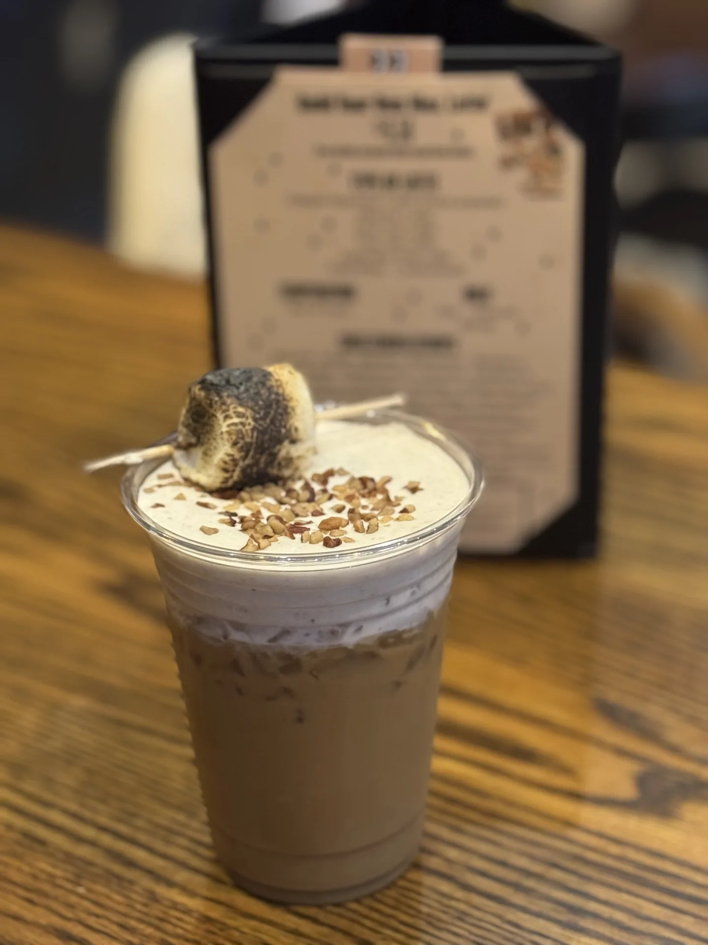 An iced latte topped with cold foam, chopped nuts, and a toasted marshmallow